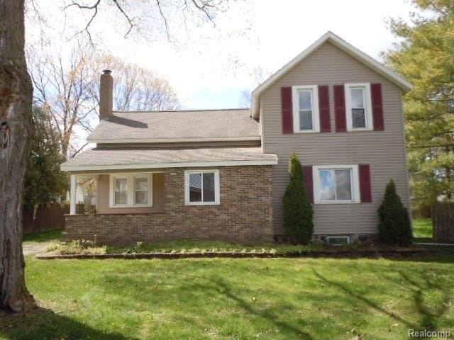 view of side of home featuring brick siding, a lawn, and a chimney