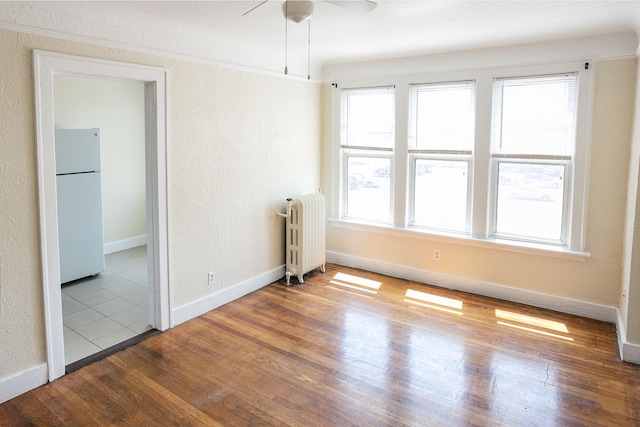 spare room featuring baseboards, a textured wall, radiator, wood-type flooring, and ceiling fan