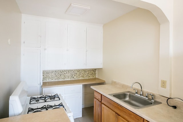 kitchen featuring arched walkways, light countertops, white cabinets, a sink, and white range with gas cooktop