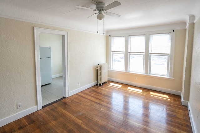 spare room with ceiling fan, a textured wall, radiator heating unit, and wood finished floors