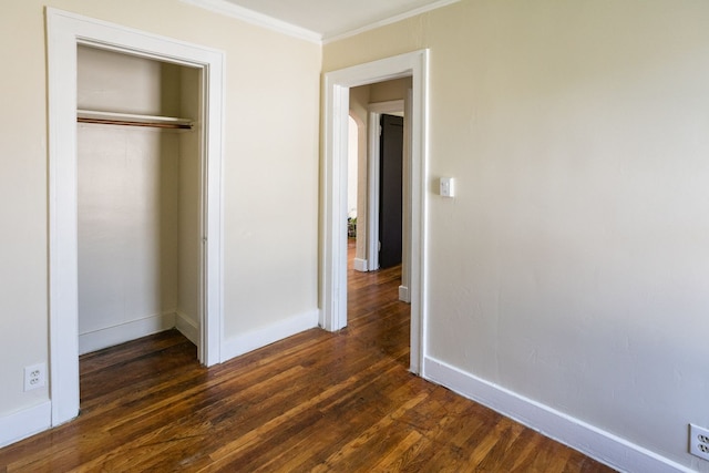 unfurnished bedroom featuring a closet, dark wood-style flooring, crown molding, and baseboards