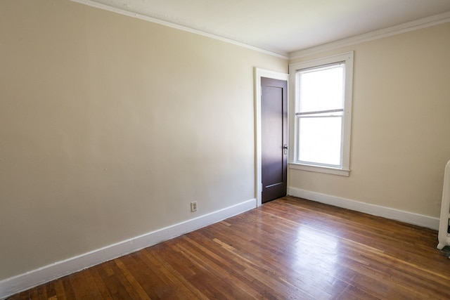 empty room featuring dark wood-type flooring, ornamental molding, and baseboards