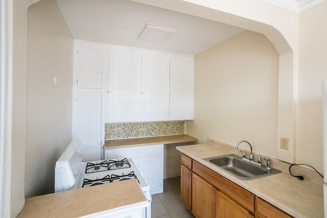 kitchen featuring arched walkways, light tile patterned floors, light countertops, white cabinets, and a sink