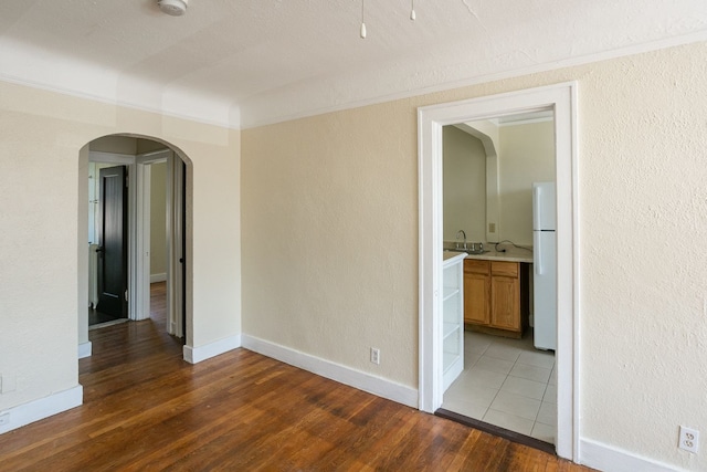 spare room featuring arched walkways, a textured wall, a sink, baseboards, and light wood-style floors