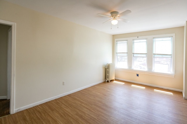 empty room with radiator, ceiling fan, baseboards, and wood finished floors