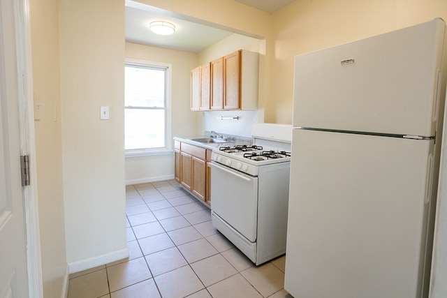 kitchen featuring light tile patterned floors, white appliances, a sink, baseboards, and light countertops