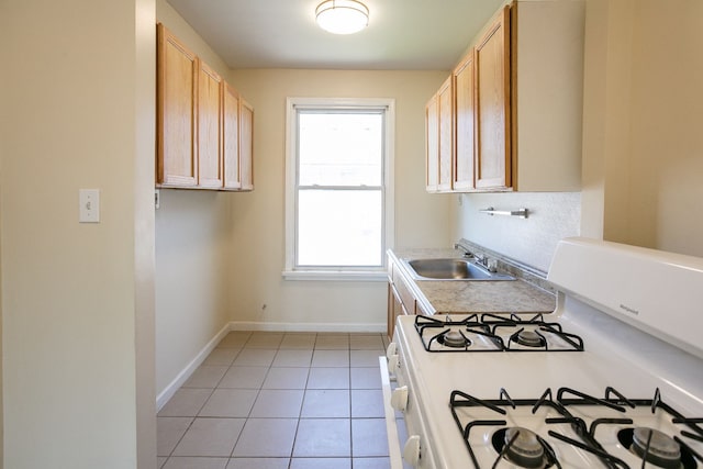 kitchen featuring light tile patterned floors, light countertops, a sink, white range with gas stovetop, and baseboards