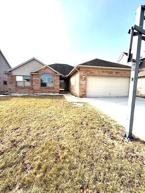 single story home with concrete driveway, brick siding, a front lawn, and an attached garage