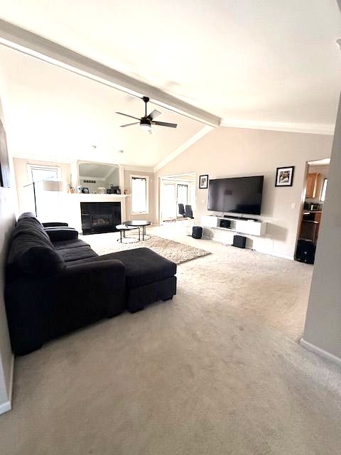 carpeted living area with a ceiling fan, a glass covered fireplace, lofted ceiling with beams, and baseboards