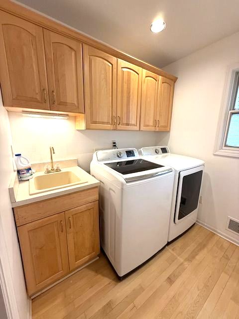 washroom with light wood-style flooring, separate washer and dryer, a sink, visible vents, and cabinet space