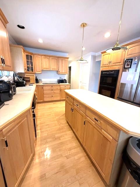 kitchen featuring pendant lighting, light wood finished floors, light countertops, dobule oven black, and glass insert cabinets