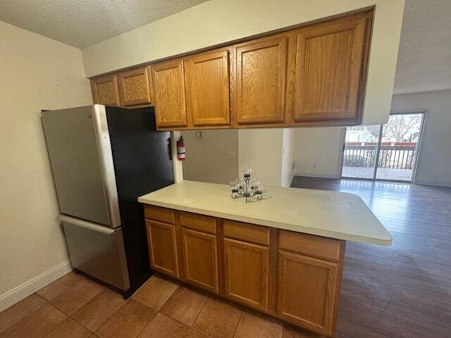 kitchen featuring light countertops, freestanding refrigerator, brown cabinets, and a peninsula