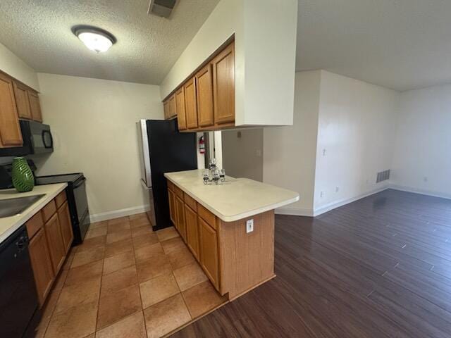 kitchen featuring a peninsula, visible vents, light countertops, black appliances, and brown cabinetry