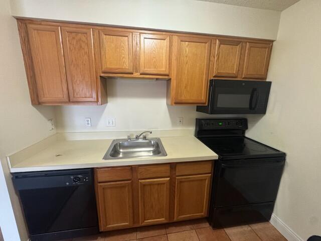 kitchen with light countertops, brown cabinets, a sink, and black appliances