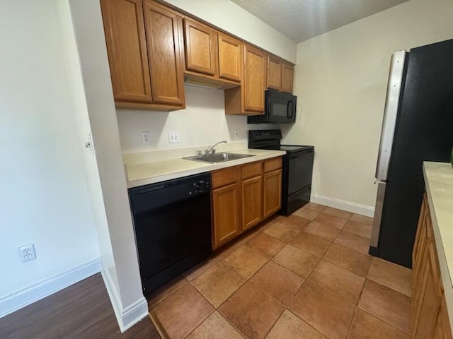 kitchen featuring baseboards, brown cabinetry, light countertops, black appliances, and a sink