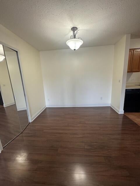 unfurnished dining area featuring a textured ceiling, dark wood-style flooring, and baseboards