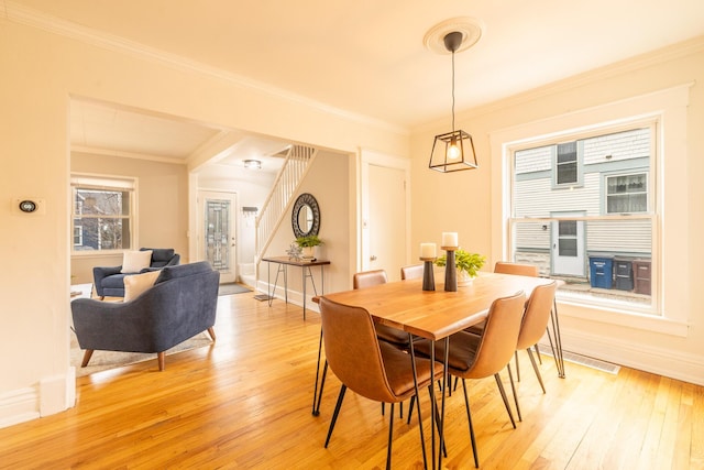 dining room with light wood-type flooring, crown molding, stairway, and baseboards