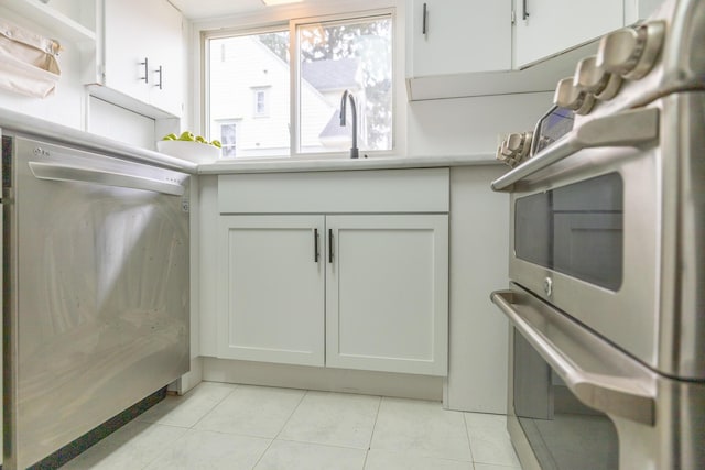 kitchen with light tile patterned flooring, stove, white cabinetry, light countertops, and dishwasher