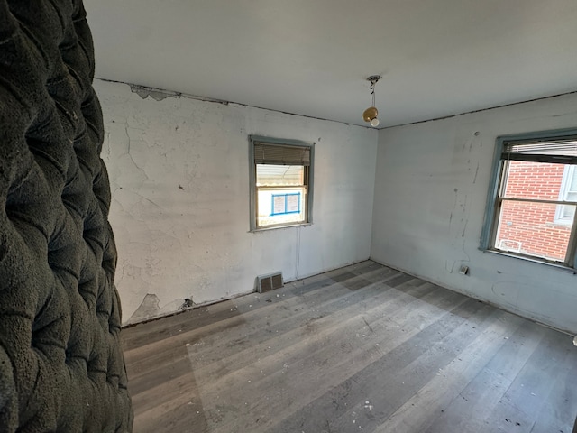 unfurnished room with a healthy amount of sunlight, visible vents, and wood finished floors