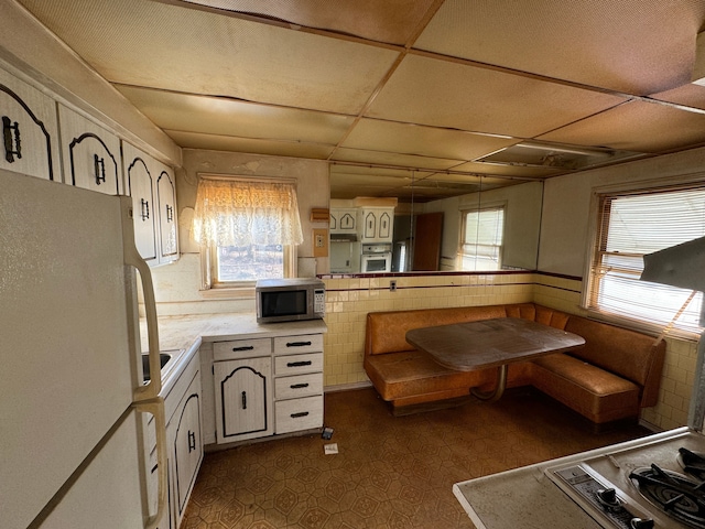 kitchen with dark floors, stainless steel appliances, light countertops, white cabinets, and a drop ceiling