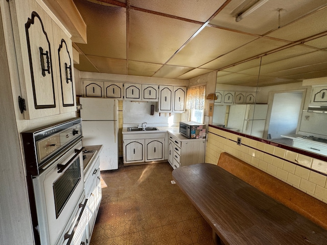 kitchen featuring dark floors, white appliances, a drop ceiling, and a sink