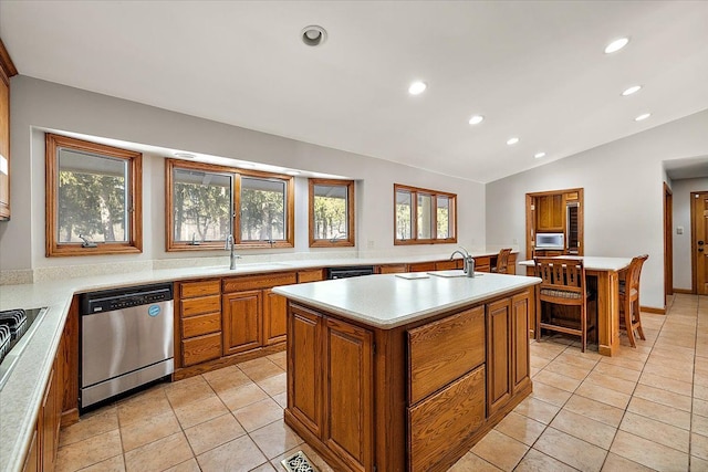 kitchen with brown cabinetry, dishwasher, a kitchen island with sink, light countertops, and a sink