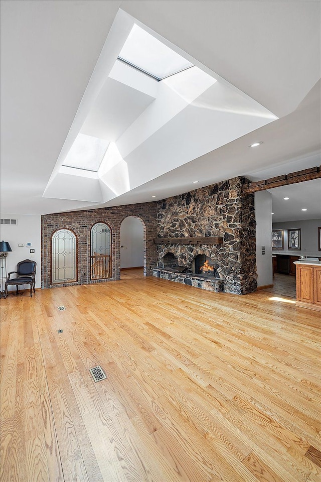 unfurnished living room with light wood-type flooring, arched walkways, visible vents, and a fireplace