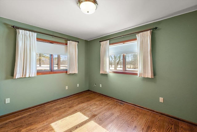 empty room featuring a wealth of natural light, baseboards, and wood finished floors