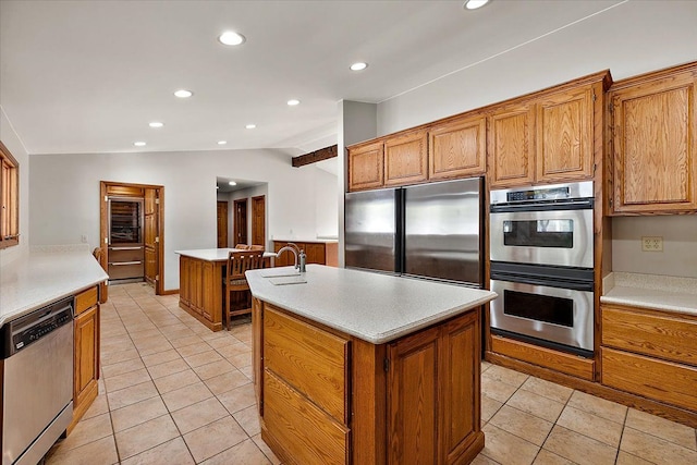 kitchen with light tile patterned floors, brown cabinets, a kitchen island with sink, vaulted ceiling, and stainless steel appliances