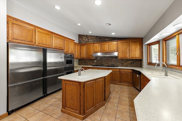 kitchen featuring brown cabinets, tasteful backsplash, lofted ceiling, appliances with stainless steel finishes, and under cabinet range hood