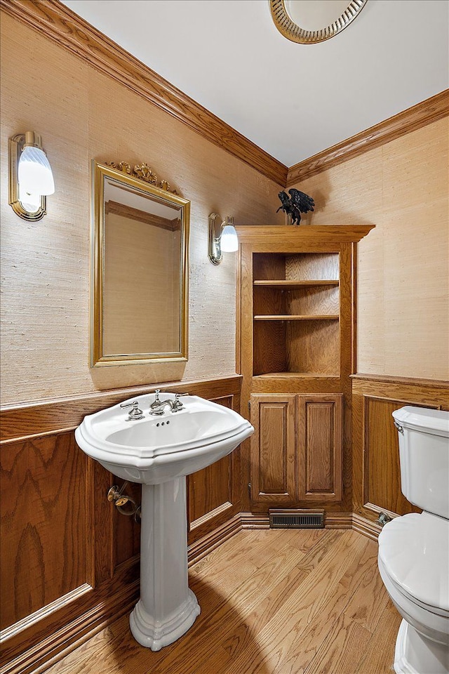 bathroom featuring toilet, wood finished floors, visible vents, ornamental molding, and wainscoting