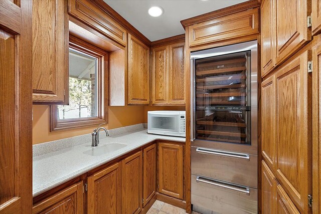 kitchen featuring white microwave, brown cabinetry, a sink, and wine cooler