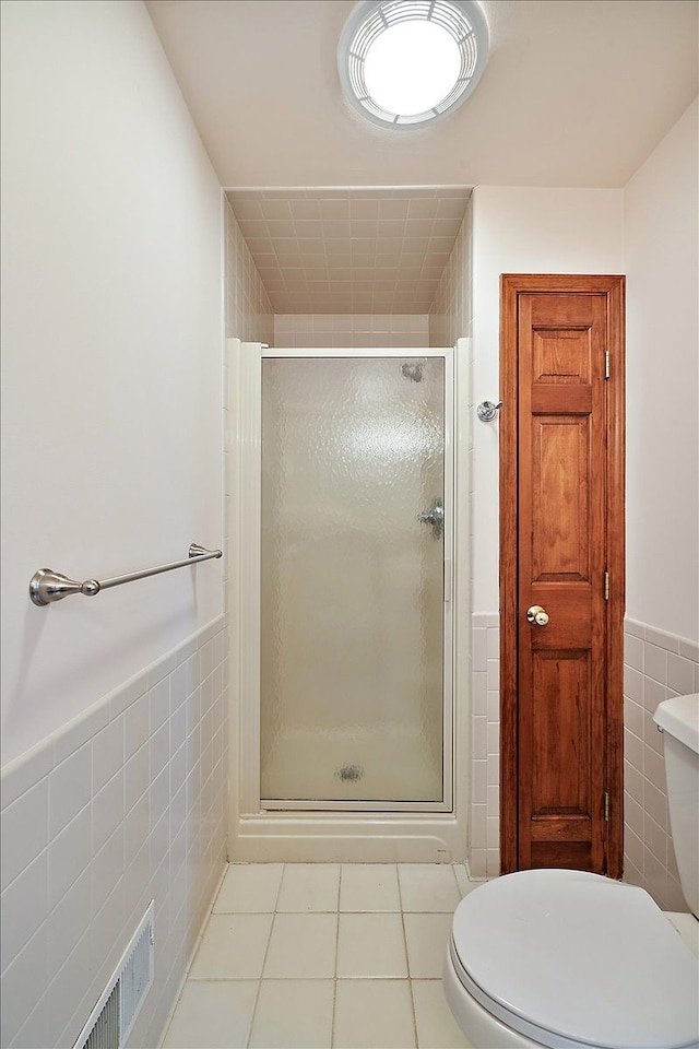 bathroom with a stall shower, visible vents, tile walls, and toilet