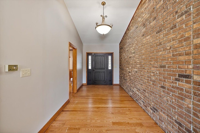 doorway with light wood-type flooring, brick wall, and baseboards