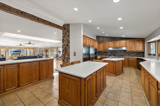 kitchen with an island with sink, brown cabinets, black refrigerator, vaulted ceiling, and under cabinet range hood