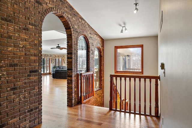 hall featuring arched walkways, brick wall, wood finished floors, and an upstairs landing