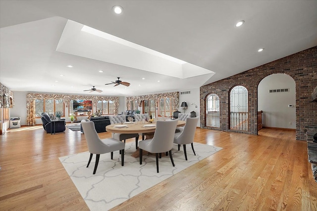 dining area featuring vaulted ceiling with skylight, visible vents, arched walkways, brick wall, and light wood-style flooring