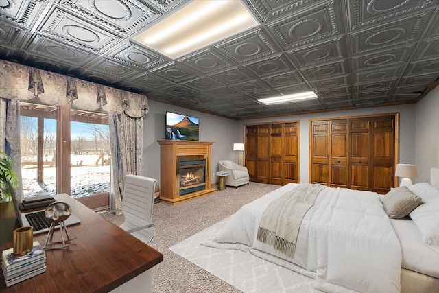 carpeted bedroom with a glass covered fireplace, an ornate ceiling, and multiple closets