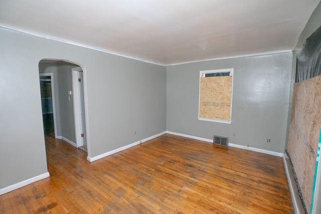 unfurnished room featuring arched walkways, visible vents, baseboards, and hardwood / wood-style flooring