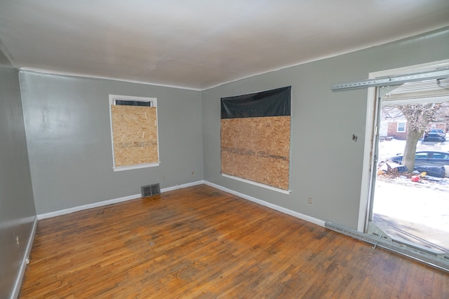 spare room featuring wood-type flooring, visible vents, and baseboards