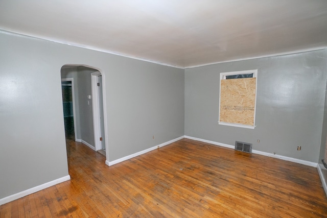 unfurnished room featuring arched walkways, visible vents, baseboards, and hardwood / wood-style flooring