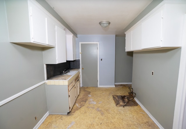 kitchen featuring a sink, baseboards, white cabinets, light countertops, and tasteful backsplash