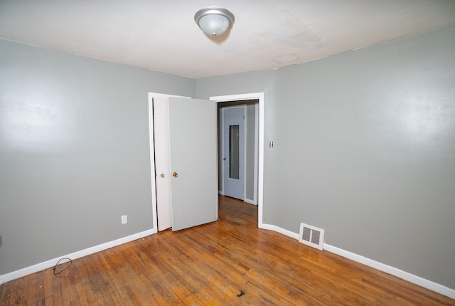 unfurnished room with wood-type flooring, visible vents, and baseboards