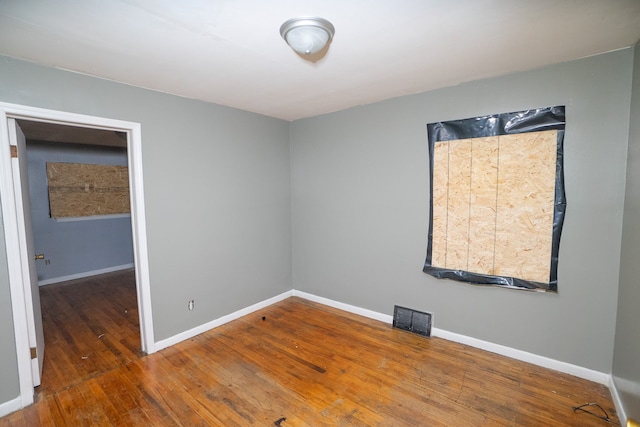 unfurnished room featuring wood-type flooring, visible vents, and baseboards