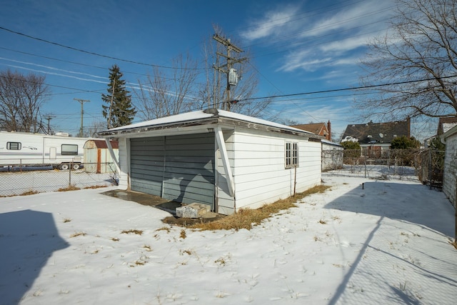 snow covered structure featuring fence and an outbuilding