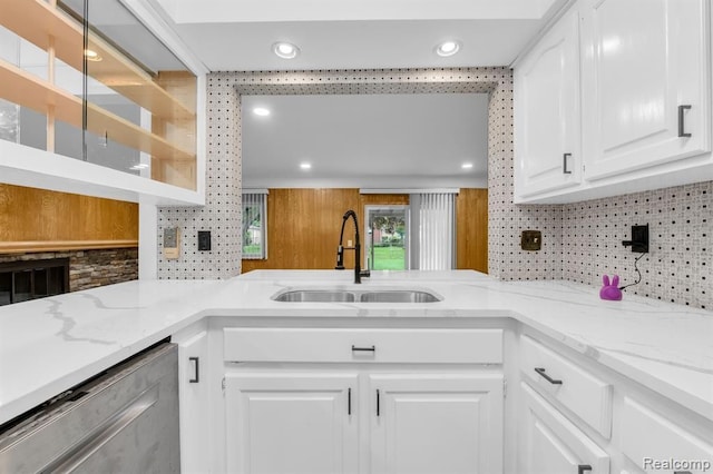 kitchen featuring a sink, white cabinets, stainless steel dishwasher, light stone countertops, and tasteful backsplash