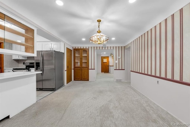 kitchen featuring pendant lighting, light countertops, light colored carpet, appliances with stainless steel finishes, and white cabinets