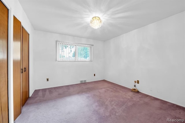 unfurnished bedroom with carpet floors, visible vents, and a notable chandelier