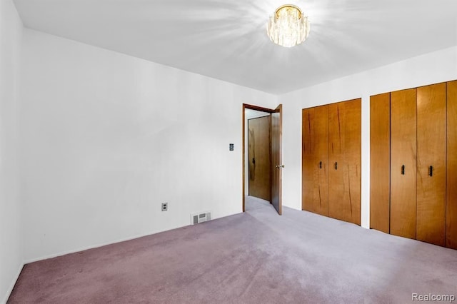 unfurnished bedroom with visible vents, two closets, and carpet flooring