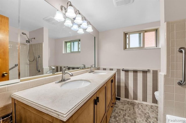 full bath with visible vents, wainscoting, a sink, and tile walls